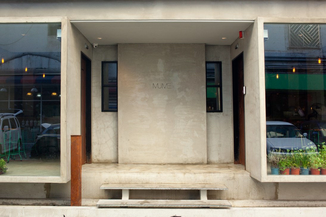 Minimalist concrete entrance to Mume restaurant with etched signage and black-framed windows