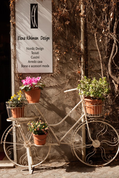 Shop exterior with Elena Kihlman Design sign and decorative bicycle with flower pots on Via Urbana in Rome's Monti neighbourhood.