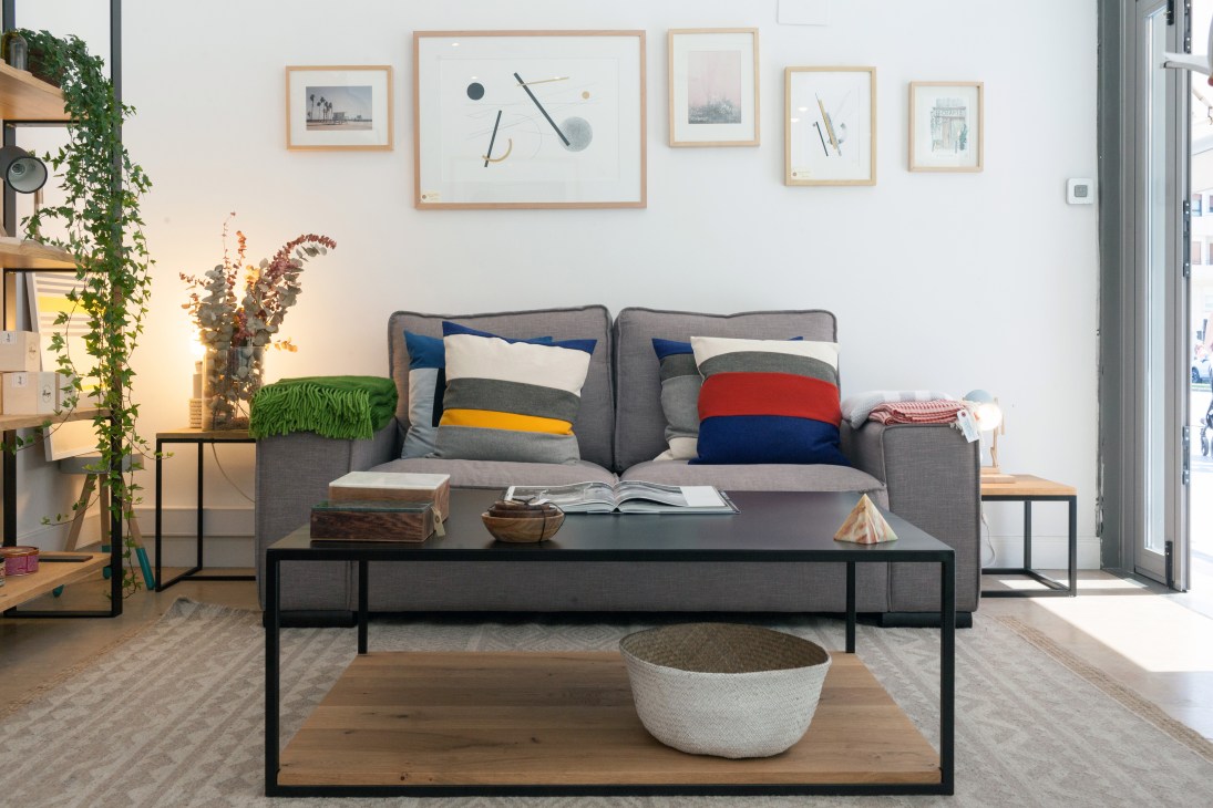 Interior of Bois Et Fer furniture showroom in San Sebastián displaying a gray sofa with colorful striped pillows and wall-mounted framed artwork.