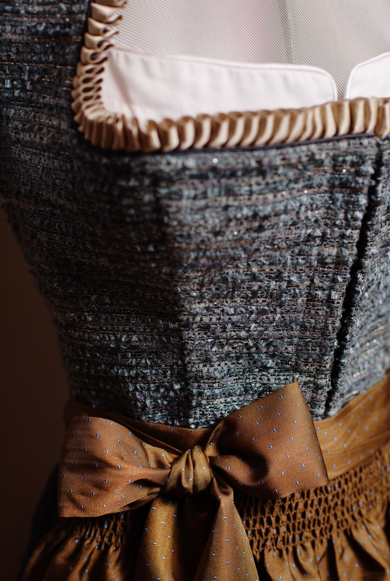 Close-up of a traditional dirndl dress with textured dark fabric, white apron, and gold bow at the waist.