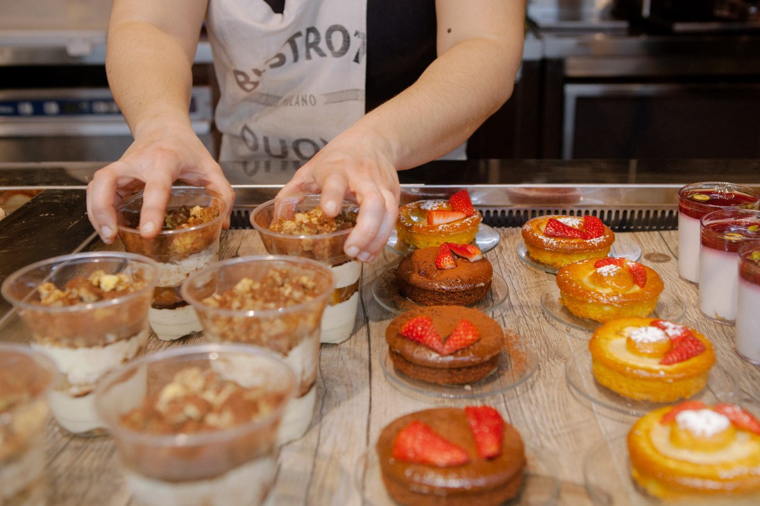A baker arranges Italian desserts on a wooden counter, including pastries topped with strawberries and powdered sugar.