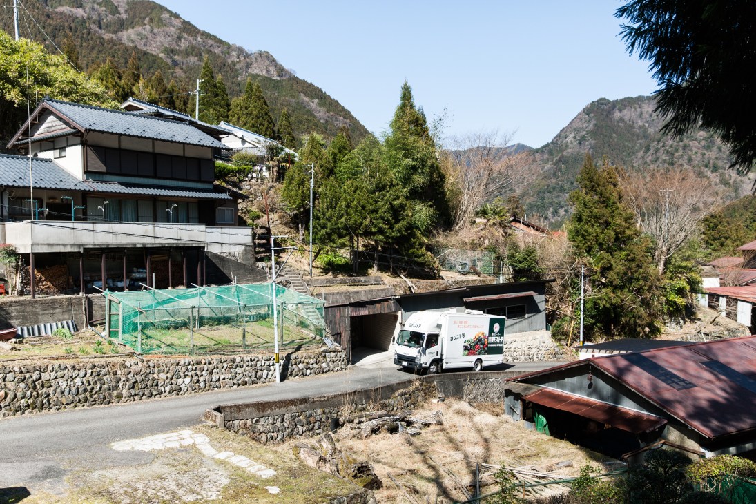 A white delivery lorry with expandable cabin navigates a mountain road near Kawakami village in Japan.