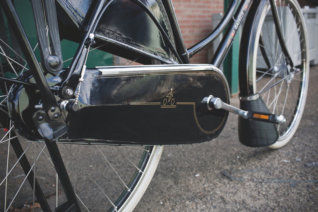 Close-up of a black Gazelle bicycle's closed chain case with gold decorative branding and bicycle icon.