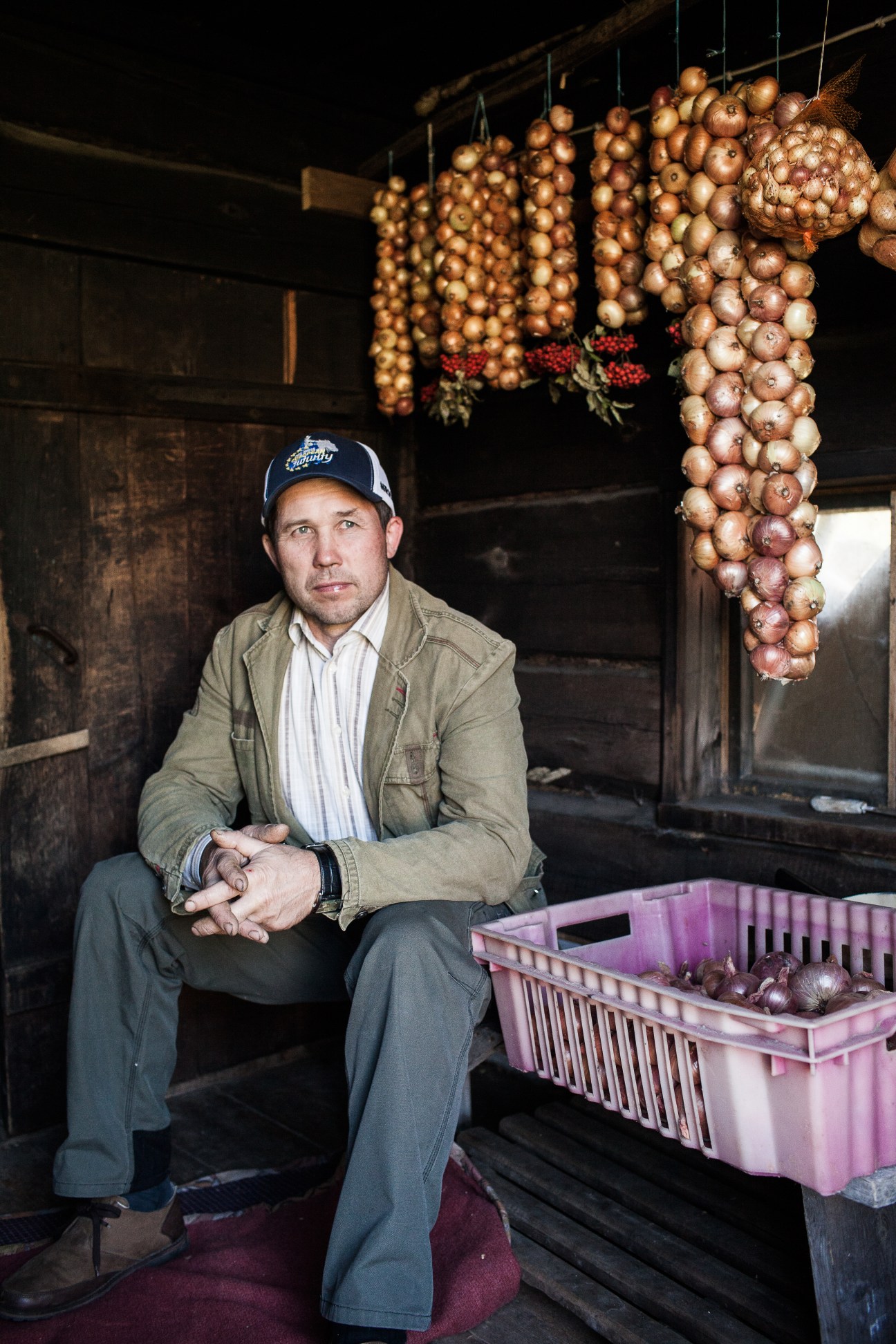 Konstantin Avvo, an onion farmer, sits in a wooden structure with braided onions hanging above him.