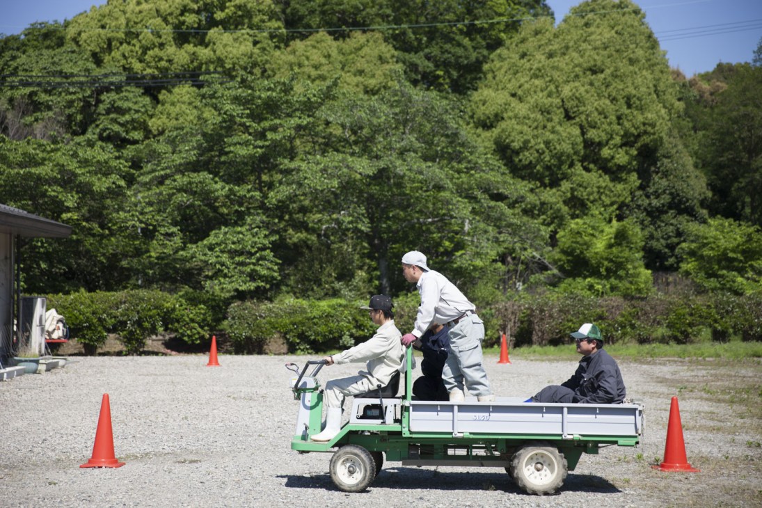 Students operating a green motorized cart at Nara Agriculture and Food International College with forested grounds in background.