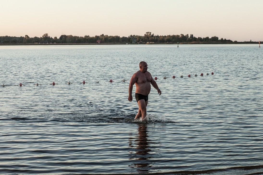 Man wading into a lake for an afternoon swim while others swim in the background.
