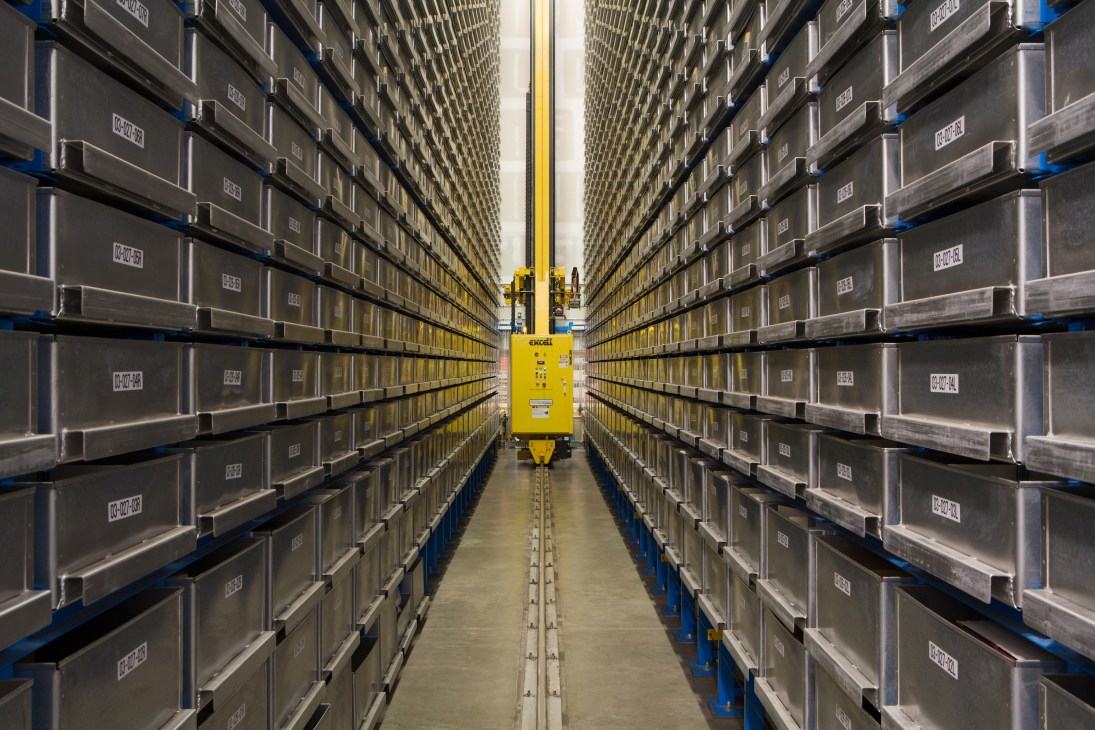 Automated tape and image archive with yellow robotic retrieval system in center aisle surrounded by metal storage bins.