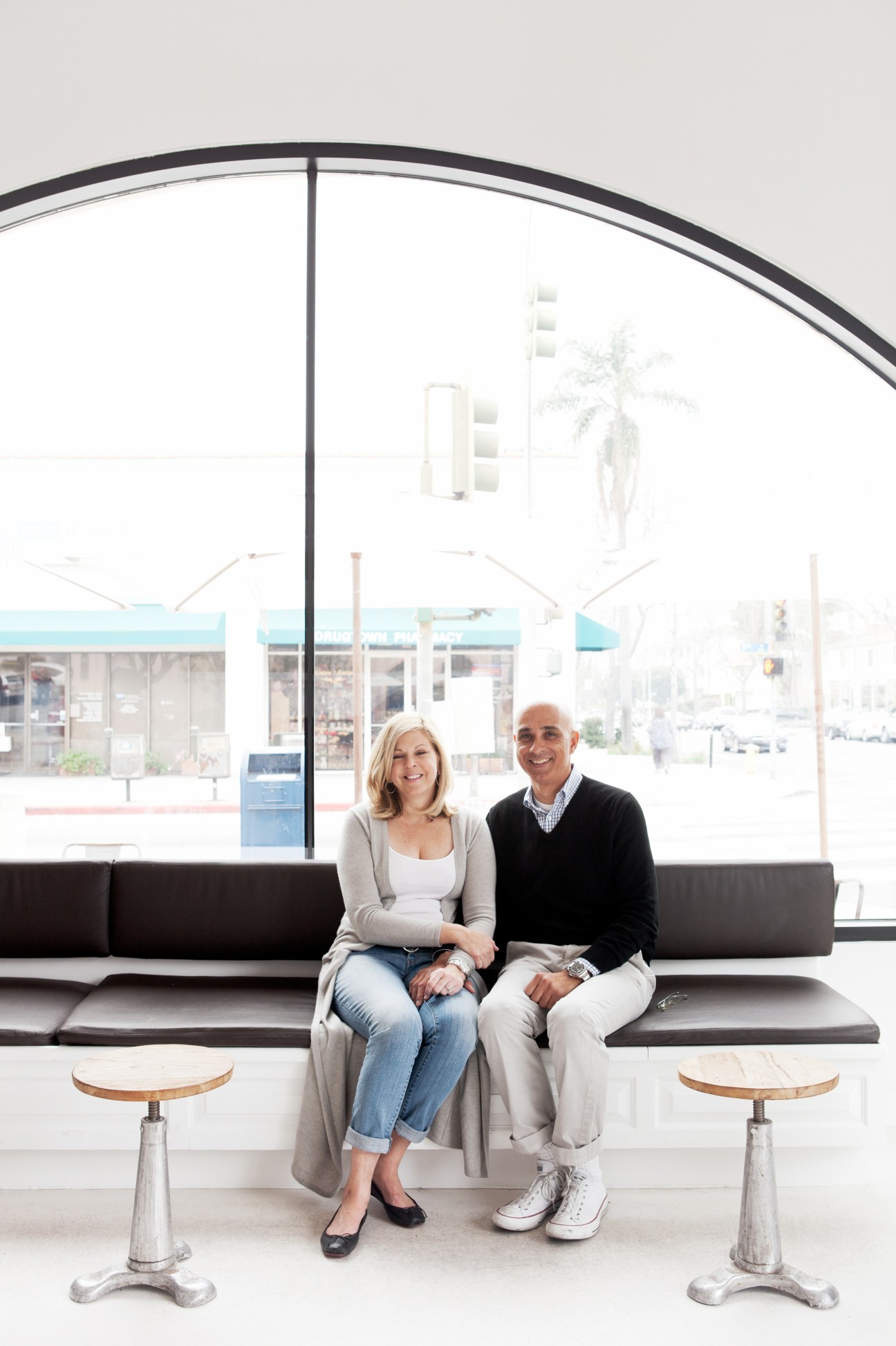 Primo Passo Coffee Co owners Stewart and Kara Bonela sit on a black bench by a large curved window.