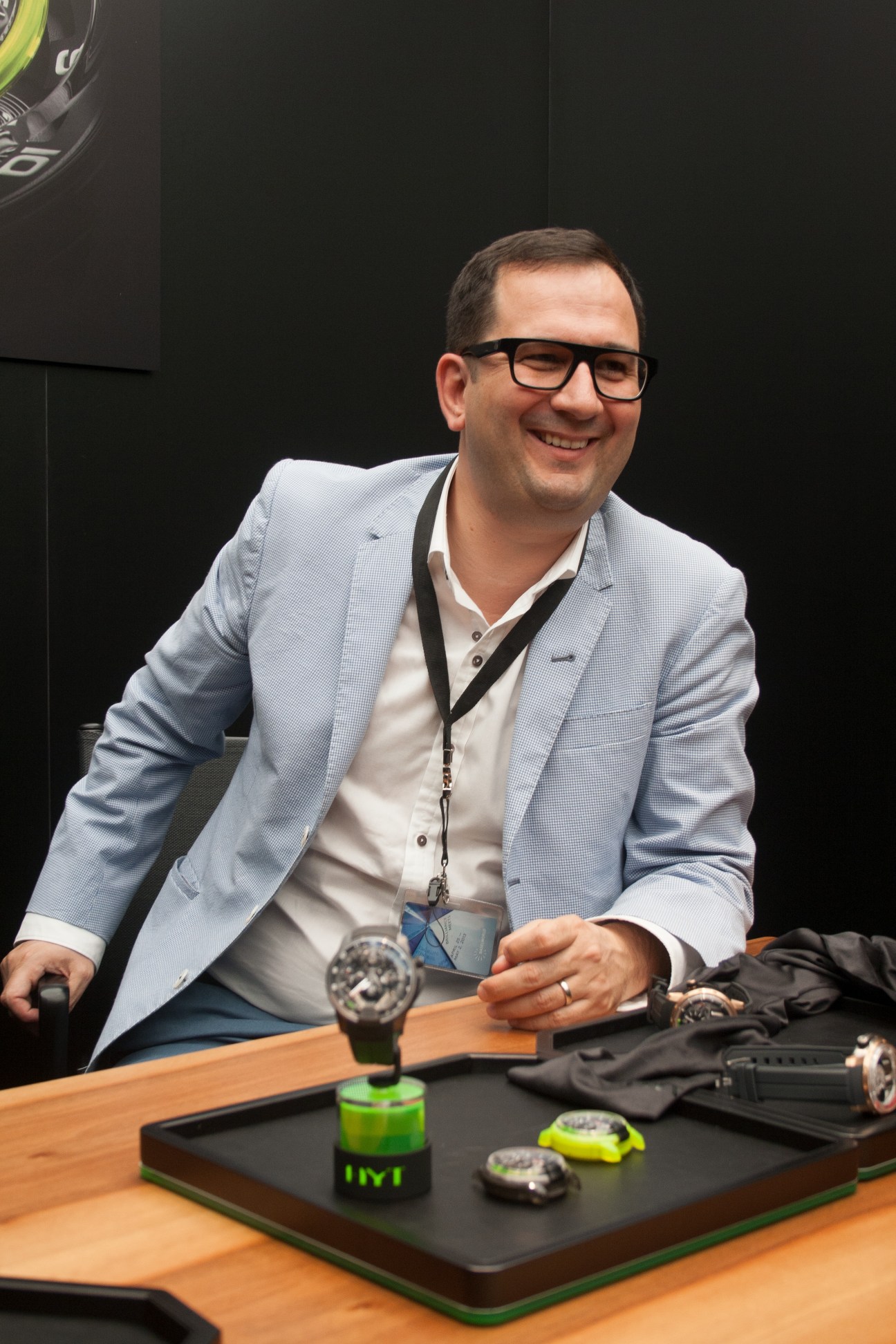 HYT Partner Ion Schiau smiling at a table displaying watches and wearing a credential lanyard.