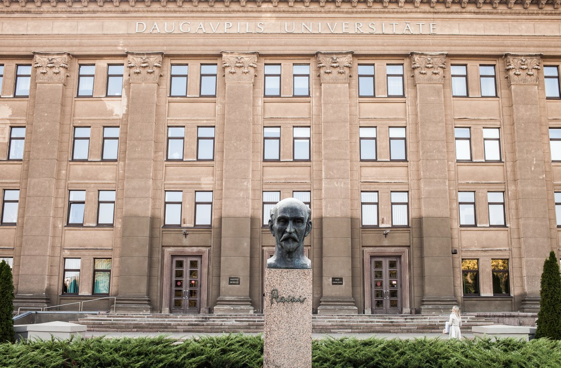Statue of Rainis, a Latvian poet, positioned in front of Daugavpils University's neoclassical building facade.