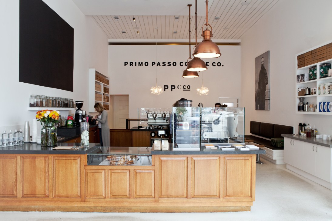 Primo Passo Coffee Co interior with wooden counter, copper pendant lights, and signage on white wall.