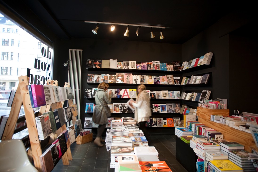 Interior of Do You Read Me?! bookstore in Berlin with customers browsing magazines on black shelving and wooden display stands.