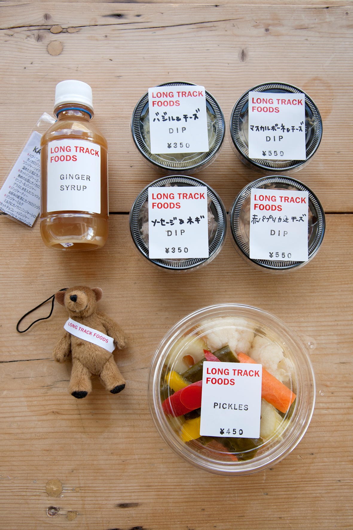 Long Track Foods products including ginger syrup, dips, pickles and a small stuffed bear on wooden surface.
