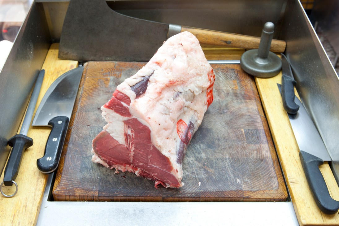 Raw meat cut displayed on a wooden cutting board with butcher knives and tools at Macelleria Annunciata.