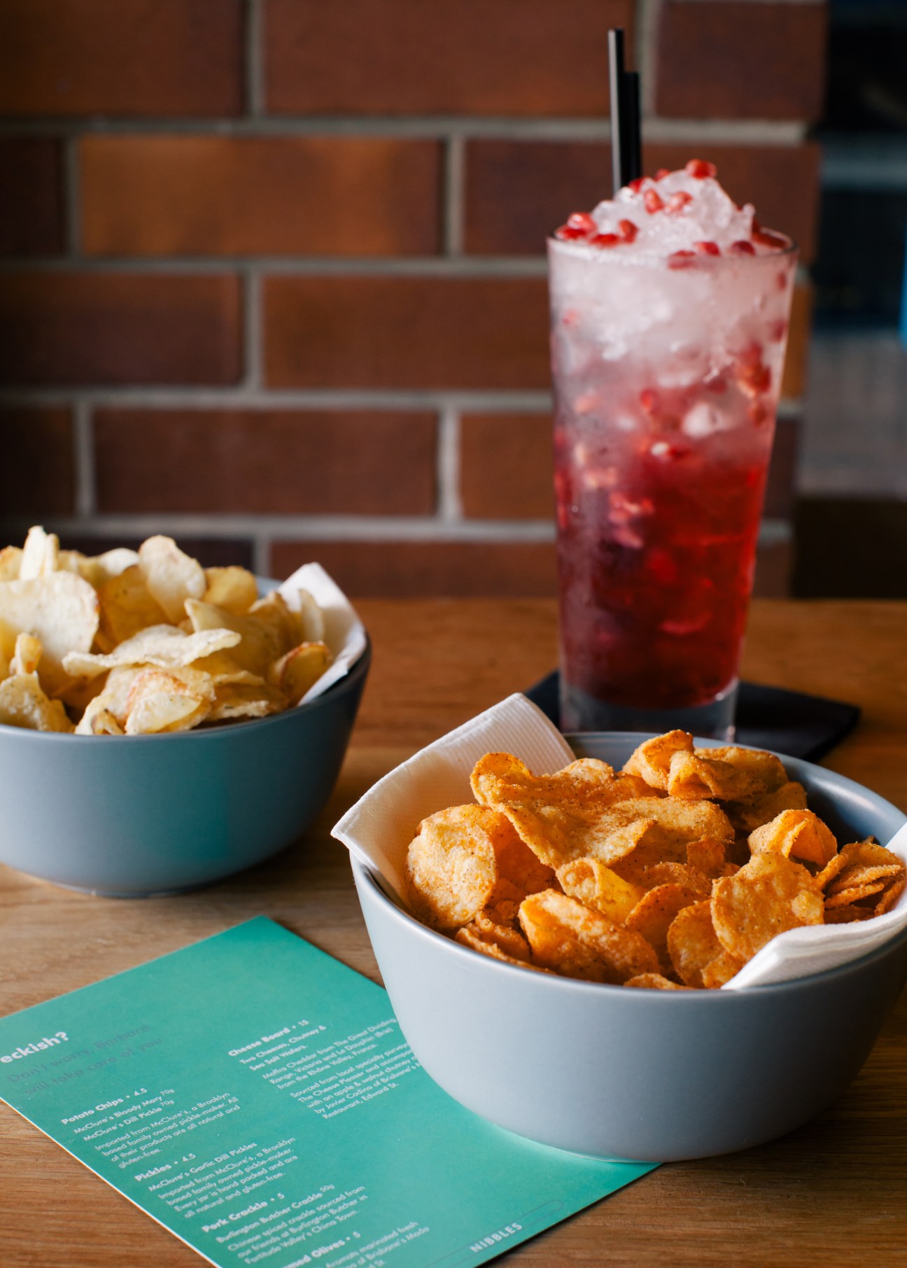 Red cocktail with ice and white foam garnish, served alongside bowls of potato chips on a wooden table at Barbara, Brisbane.