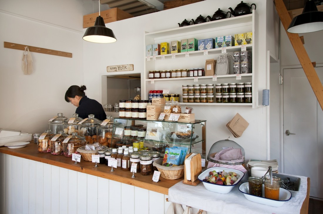Interior of Long Track Foods shop in Kamakura showing shelves stocked with jars, teapot covers, and artisanal products with a staff member behind counter.