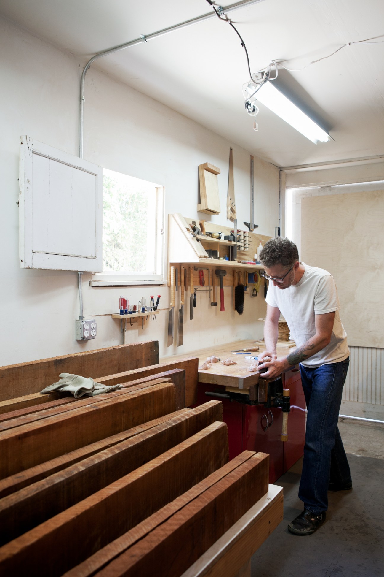 Woodworker in studio workshop hand-carving wooden furniture pieces at workbench.