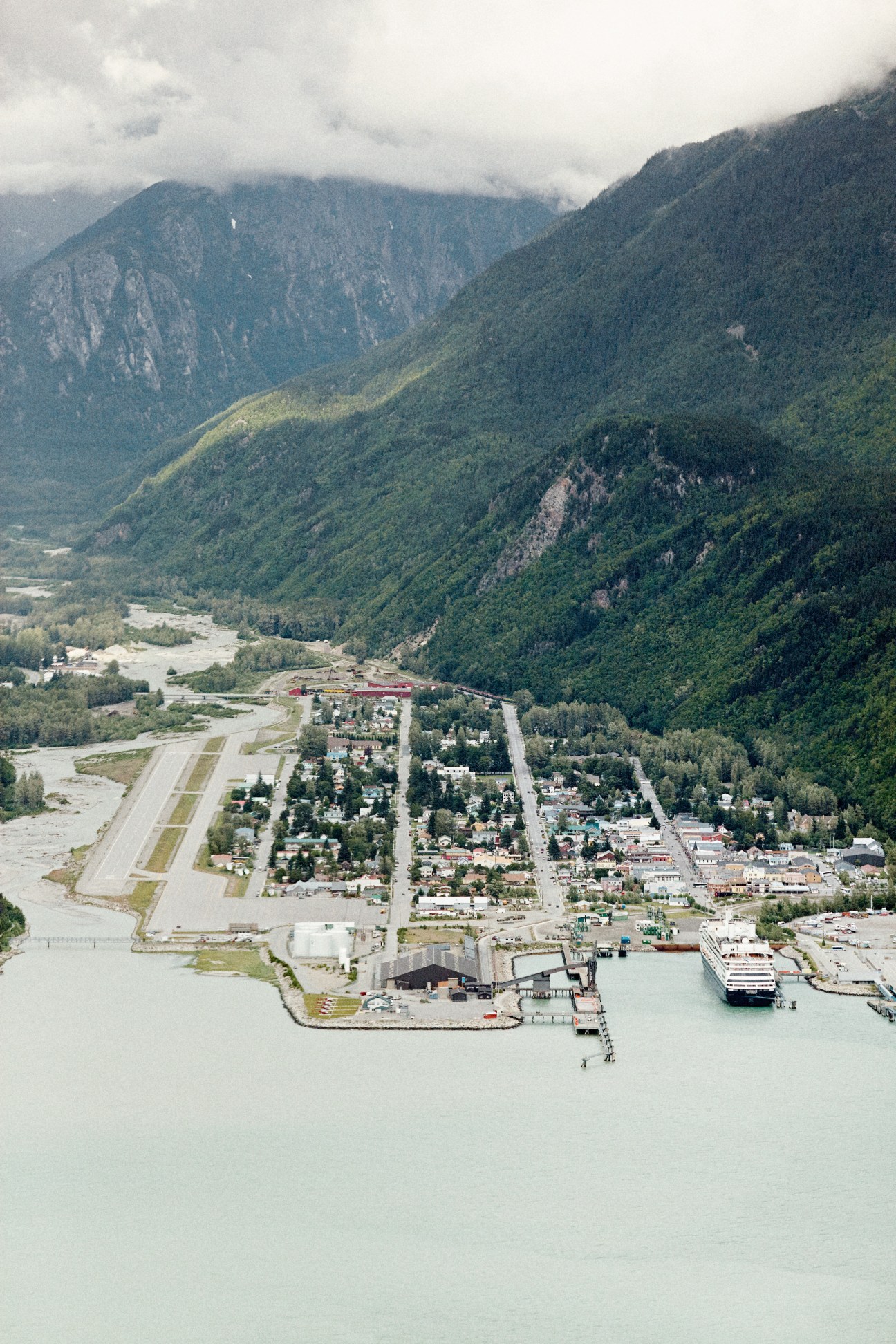 Aerial view of Skagway, Alaska nestled in a valley surrounded by forested mountains with a ferry terminal visible at the waterfront.
