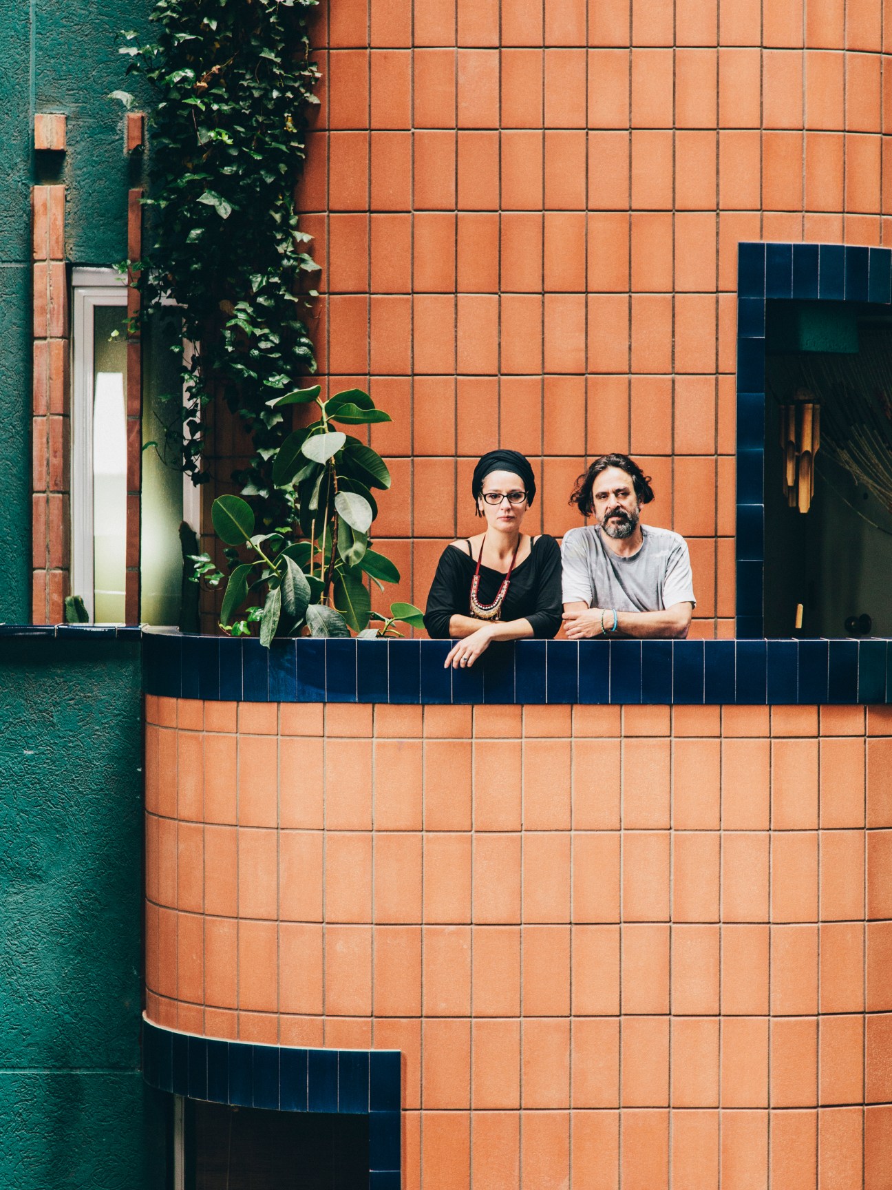 Two residents stand on a curved balcony against Walden 7's terracotta brick and turquoise facade.