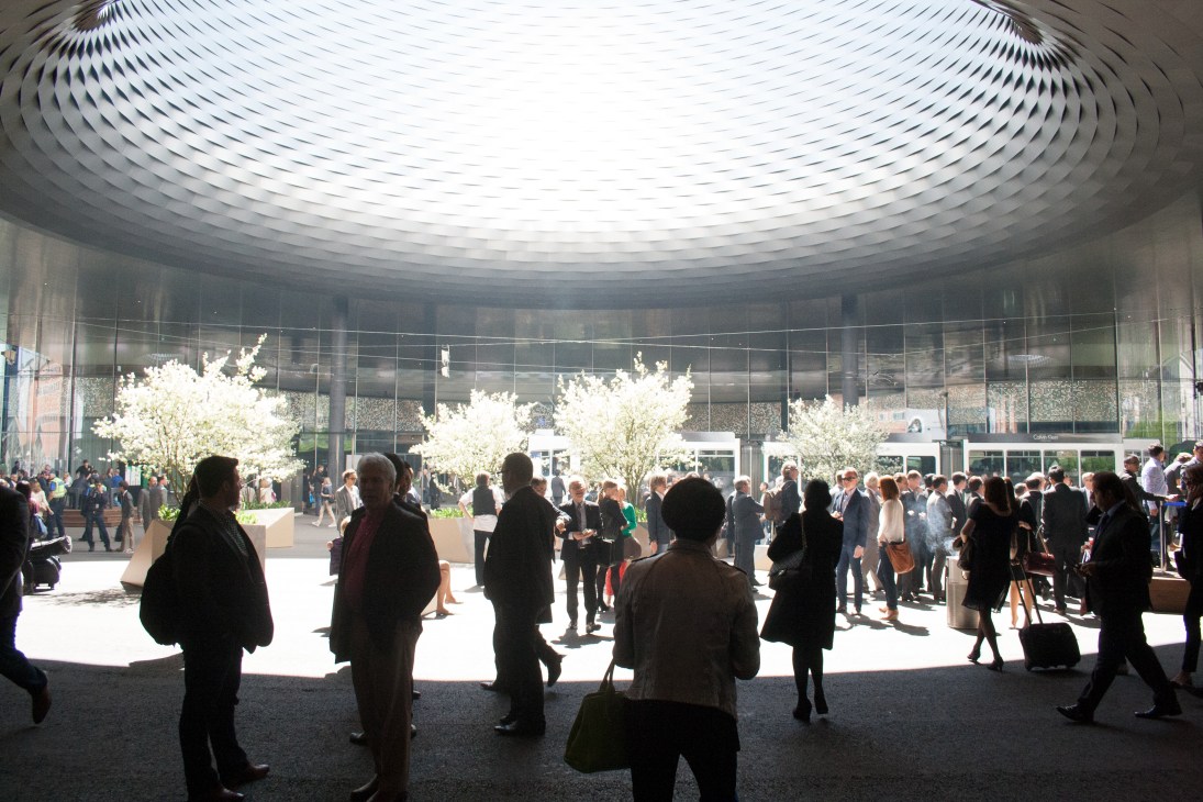 Interior atrium of Baselworld showground by Herzog & de Meuron with circular ceiling, flowering trees, and visitors.