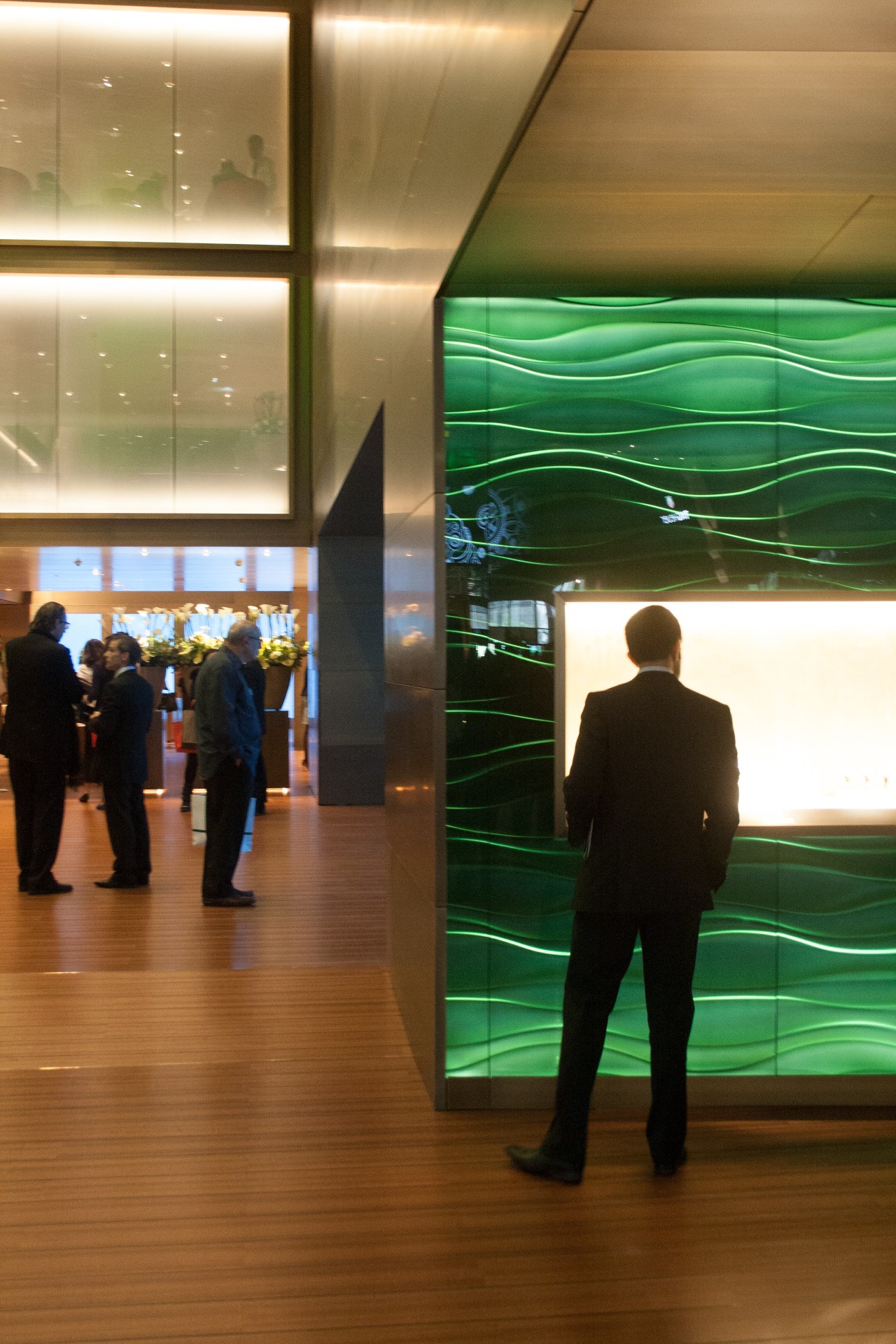 Man in suit viewing Rolex stand with green illuminated display at Baselworld trade fair.