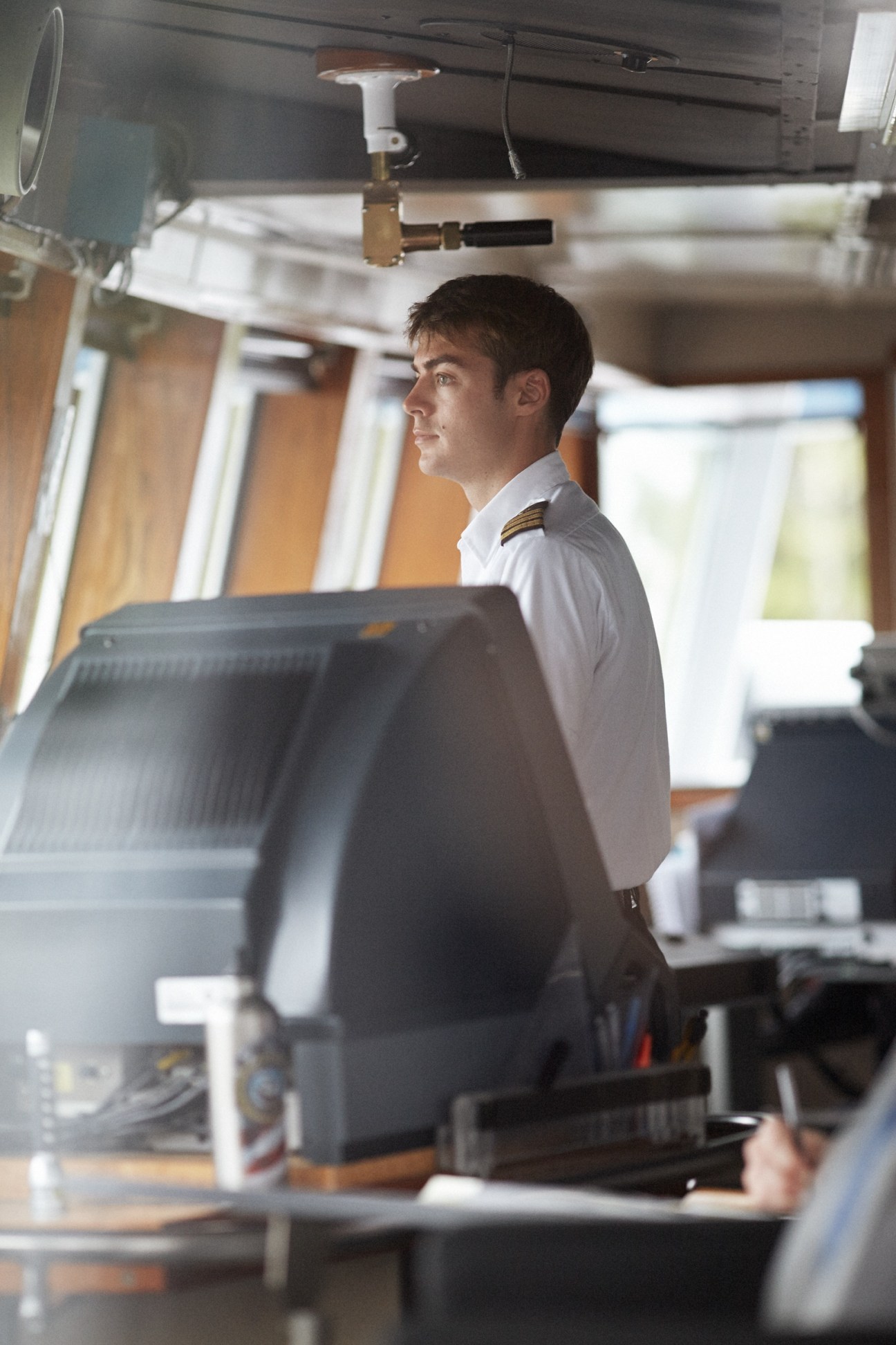 Young ferry pilot Gabriel Baylous in white uniform with gold shoulder boards stands at the helm of the M/V Columbia.
