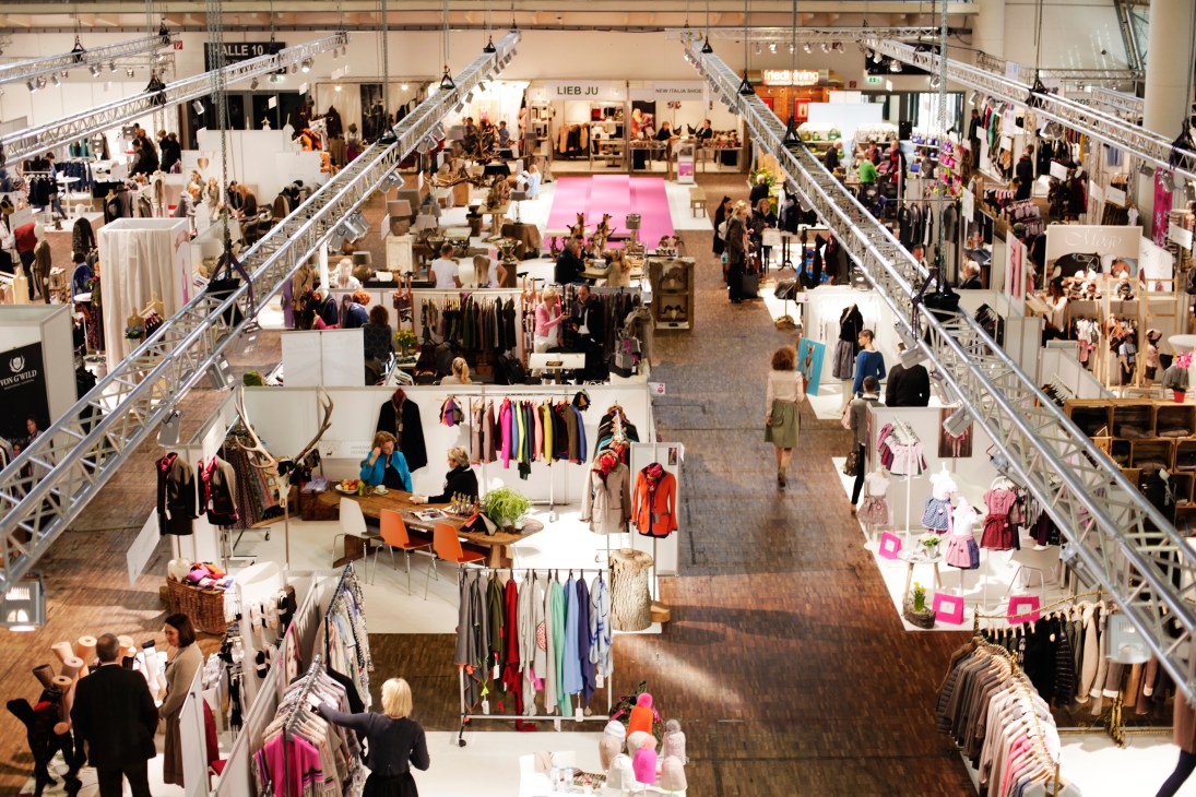 Overhead view of the Tracht & Country fair exhibition floor with white vendor booths, clothing displays, and visitors walking through halls.