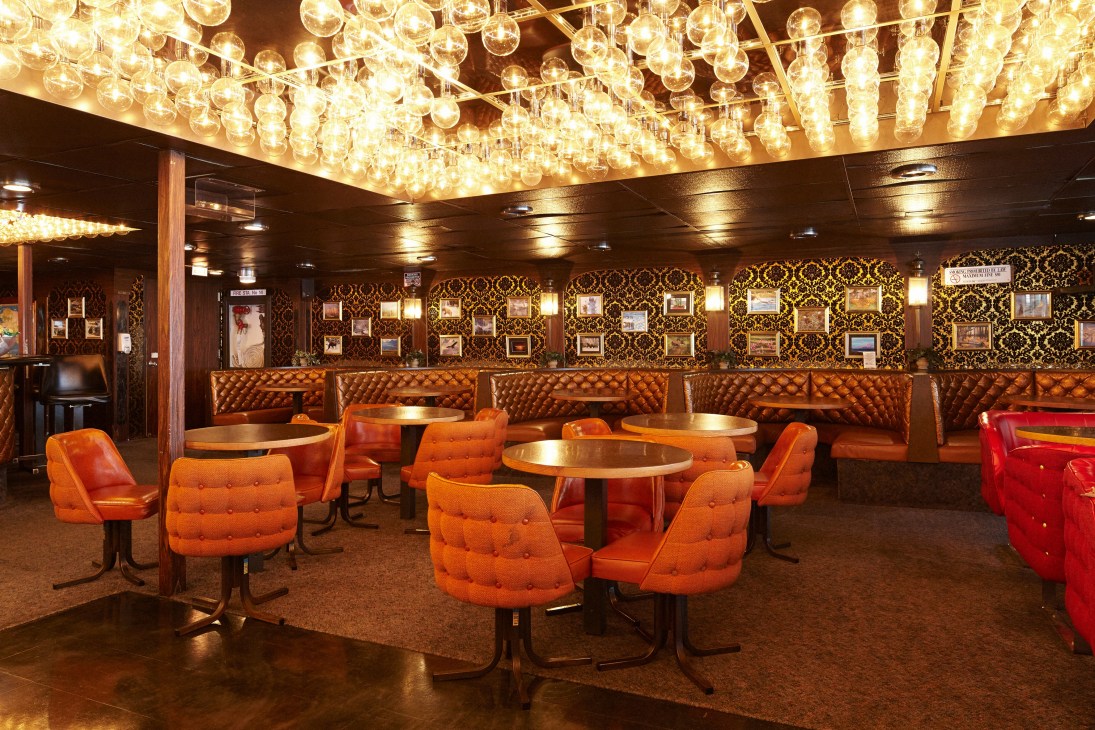 The M/V Columbia's cocktail lounge with retro 1970s decor, featuring orange velveteen chairs, paisley paneling, and hundreds of hanging vanity bulbs.