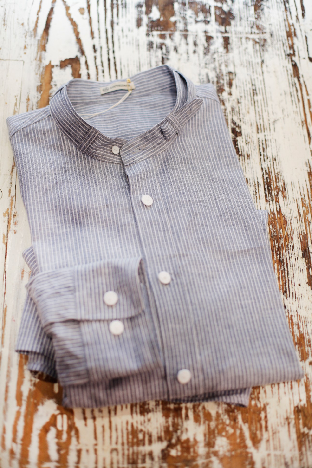 Folded light blue striped shirt by Gottseidank on a weathered white wooden surface