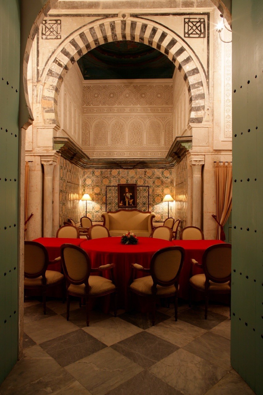 Interior of Dar Hamouda Pacha restaurant with ornate arches, decorated walls, and red-clothed dining table.