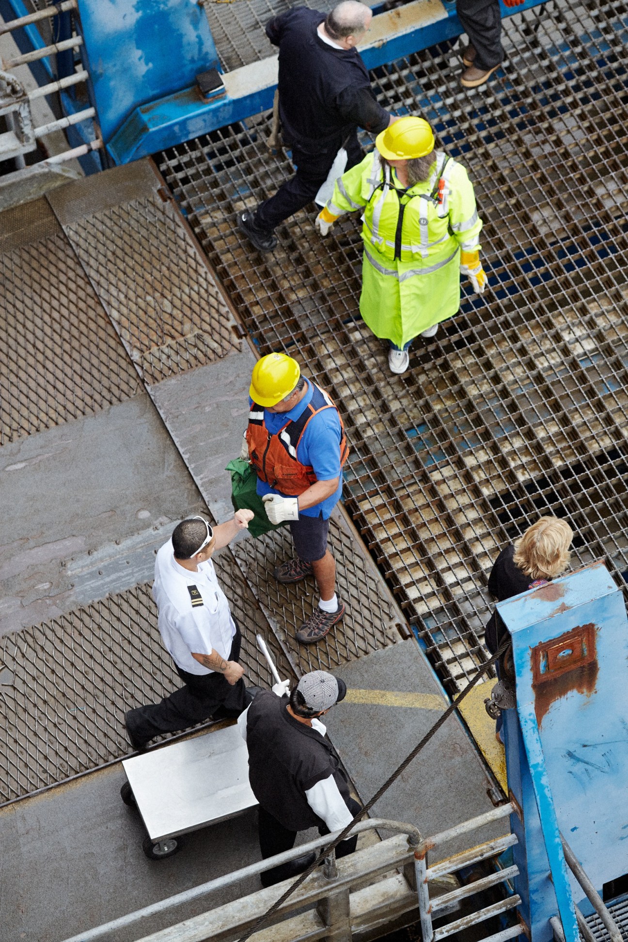 Ferry terminal crew members in safety gear securing a vehicle ramp at the dock.