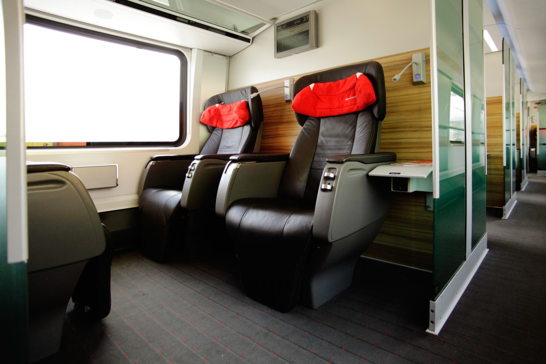 ÖBB Railjet business-class cabin with black leather reclining seats and red headrest covers.