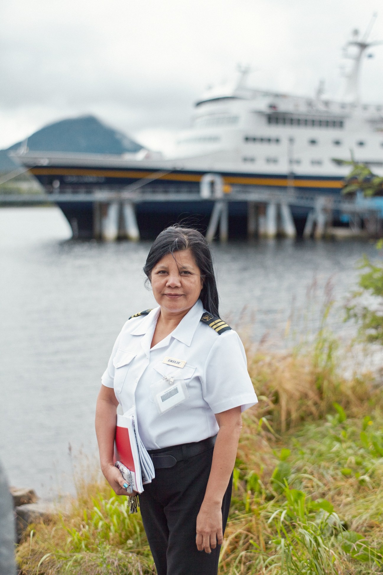 Chief steward Emelie Karline in uniform standing by the water with M/V Columbia ferry docked behind her.