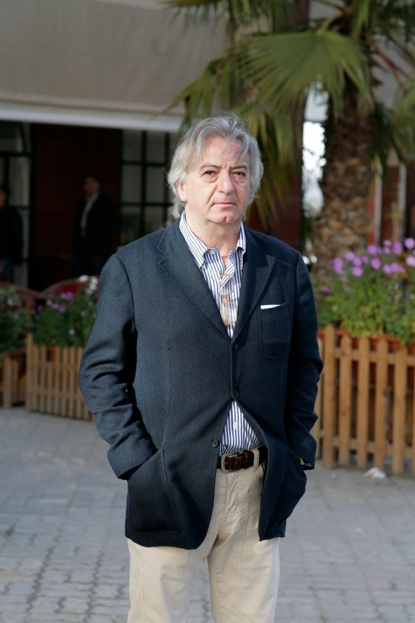 Italian expat Claudio Muccio stands in a courtyard with palm trees and flowering plants behind him.