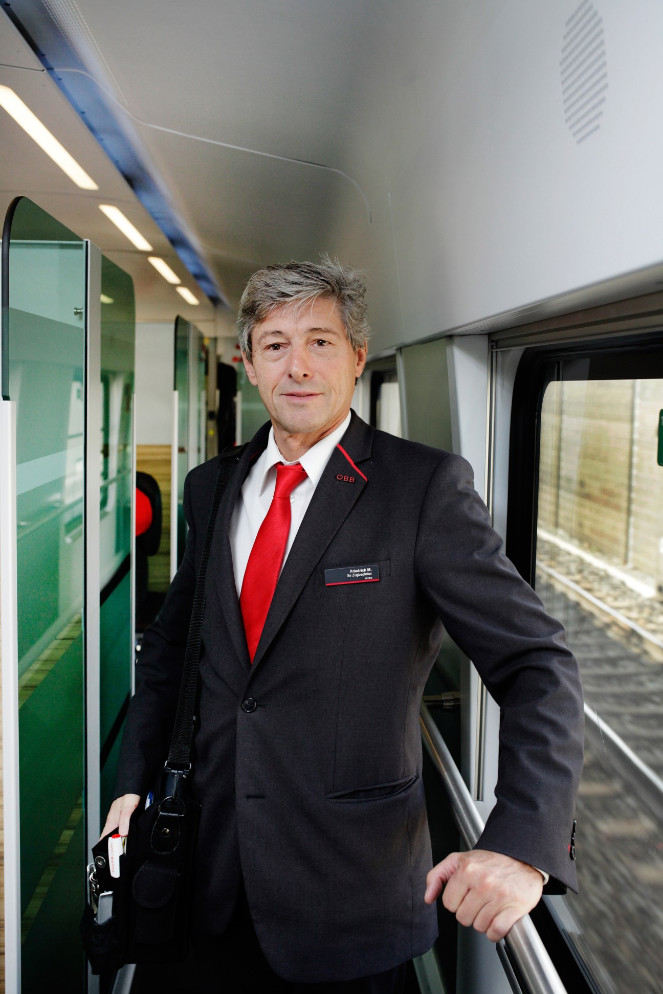 ÖBB train conductor in uniform standing in Railjet service corridor.