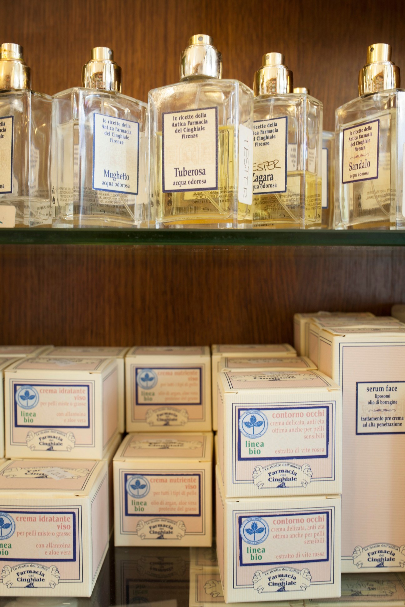 Shelves displaying Farmacia del Cinghiale's natural products including perfumes, face lotions and soaps in vintage-style glass bottles and cream-colored boxes.