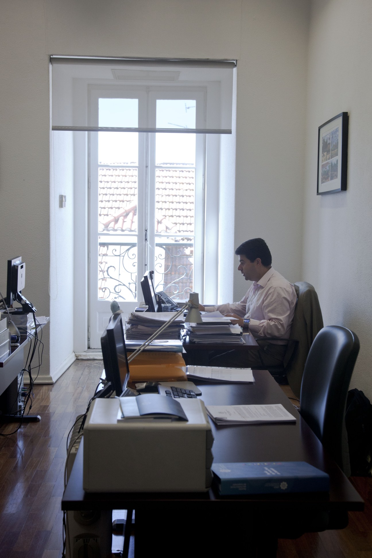 CPLP staff member working at desk in bright office with large windows overlooking Lisbon.