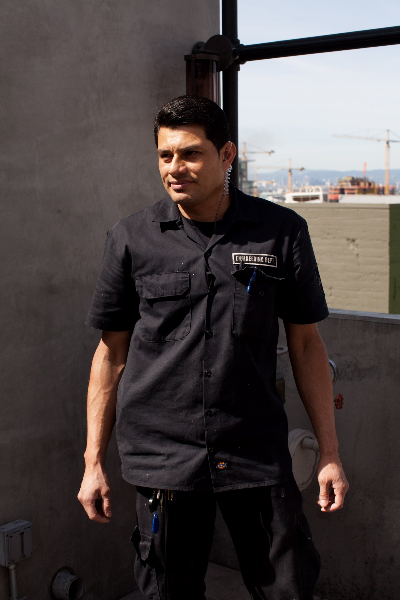Orlando Noe Perdomo, engineering representative at Ace Hotel, wearing black work shirt on rooftop with Los Angeles construction in background.