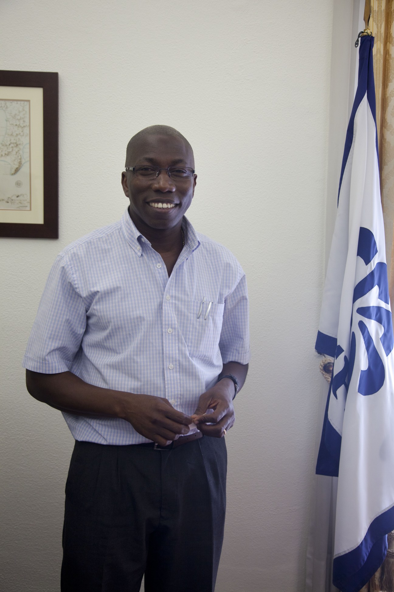 Domingos Simões Pereira, the CPLP's outgoing executive director, smiling in front of the CPLP flag.