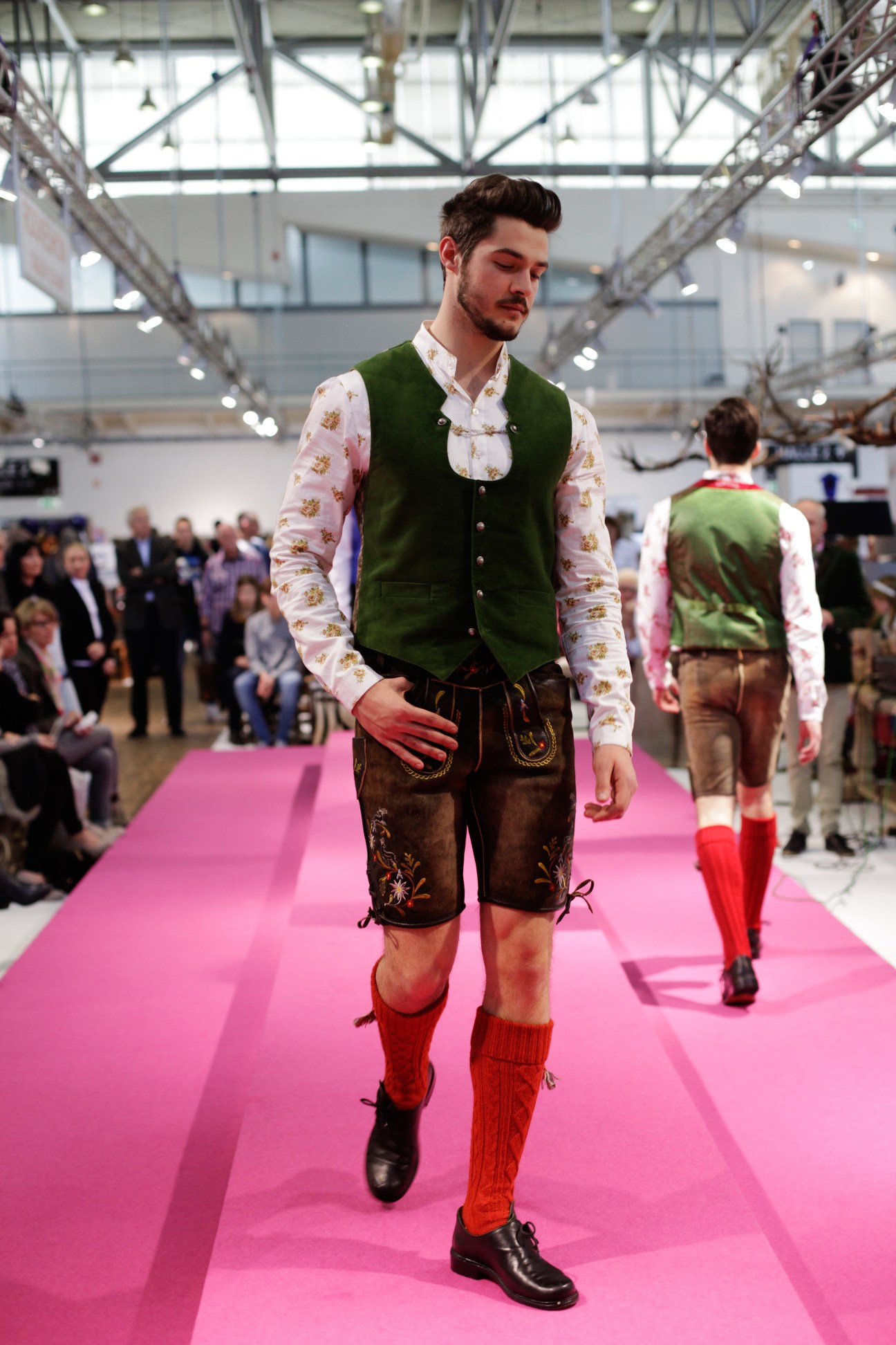 Male model wearing traditional alpine tracht ensemble on pink runway at fashion show.