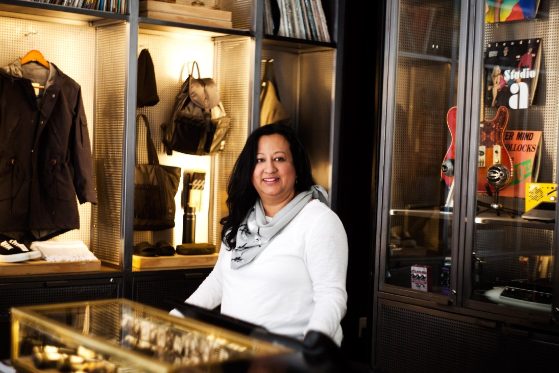 Sandra L Arbizu, human resources manager at Ace Hotel, standing in front of illuminated display cases showing clothing and accessories.