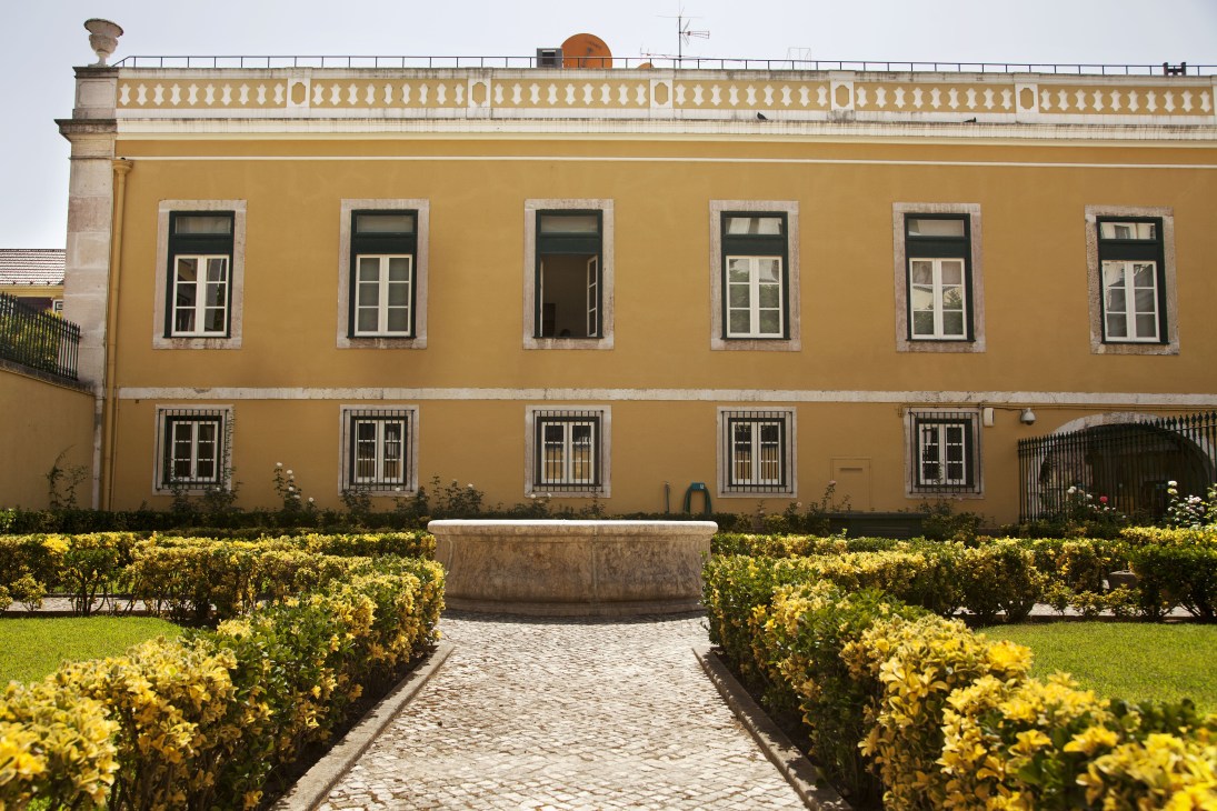 Yellow-ochre palace facade with white-trimmed windows and formal garden with yellow flowering hedges.