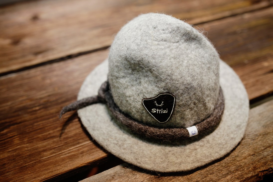 Strizi alpine hat in grey felt with dark brown cord band and black logo badge on wooden surface.