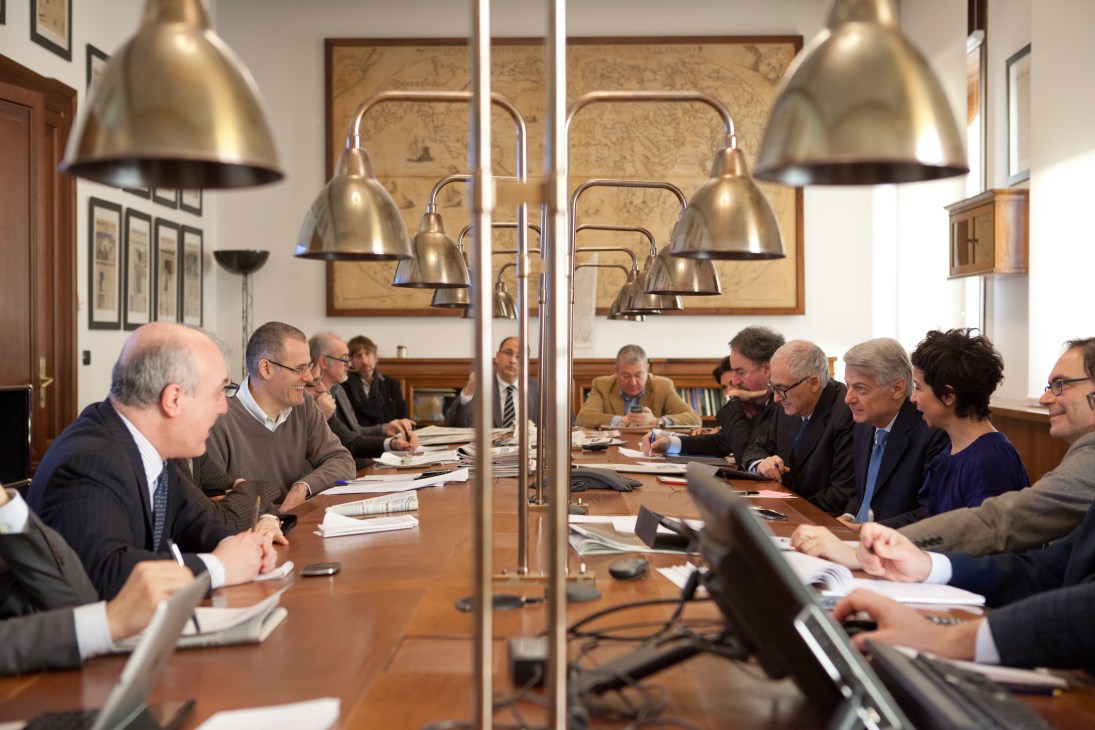 Editorial staff gathered around a wooden conference table during a meeting at Corriere della Sera newspaper.