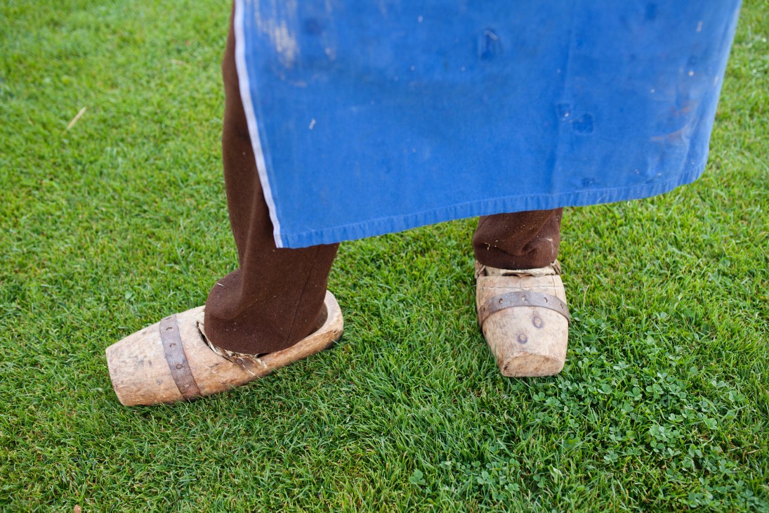 Person wearing traditional wooden clogs standing on green grass with blue fabric garment