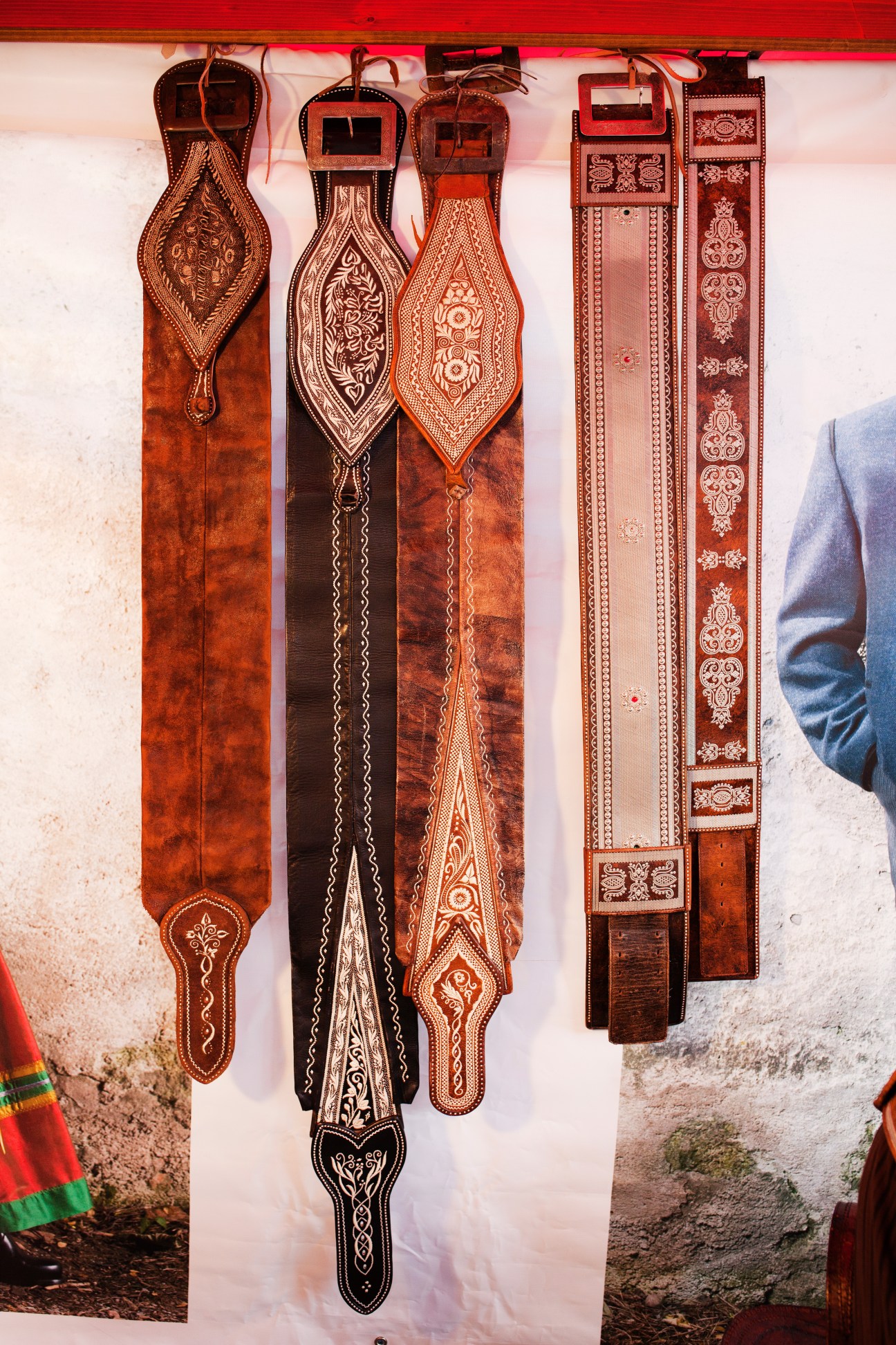 Traditional leather belts with intricate carved patterns hanging from a wooden display rack