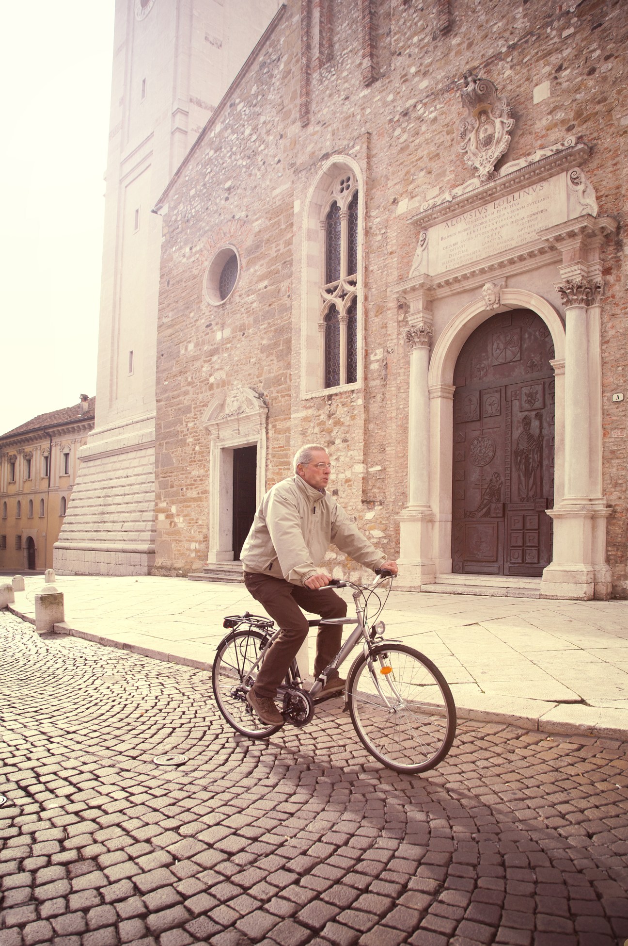 Man riding a bicycle in front of a historic brick cathedral with ornate doors in Belluno, Italy.