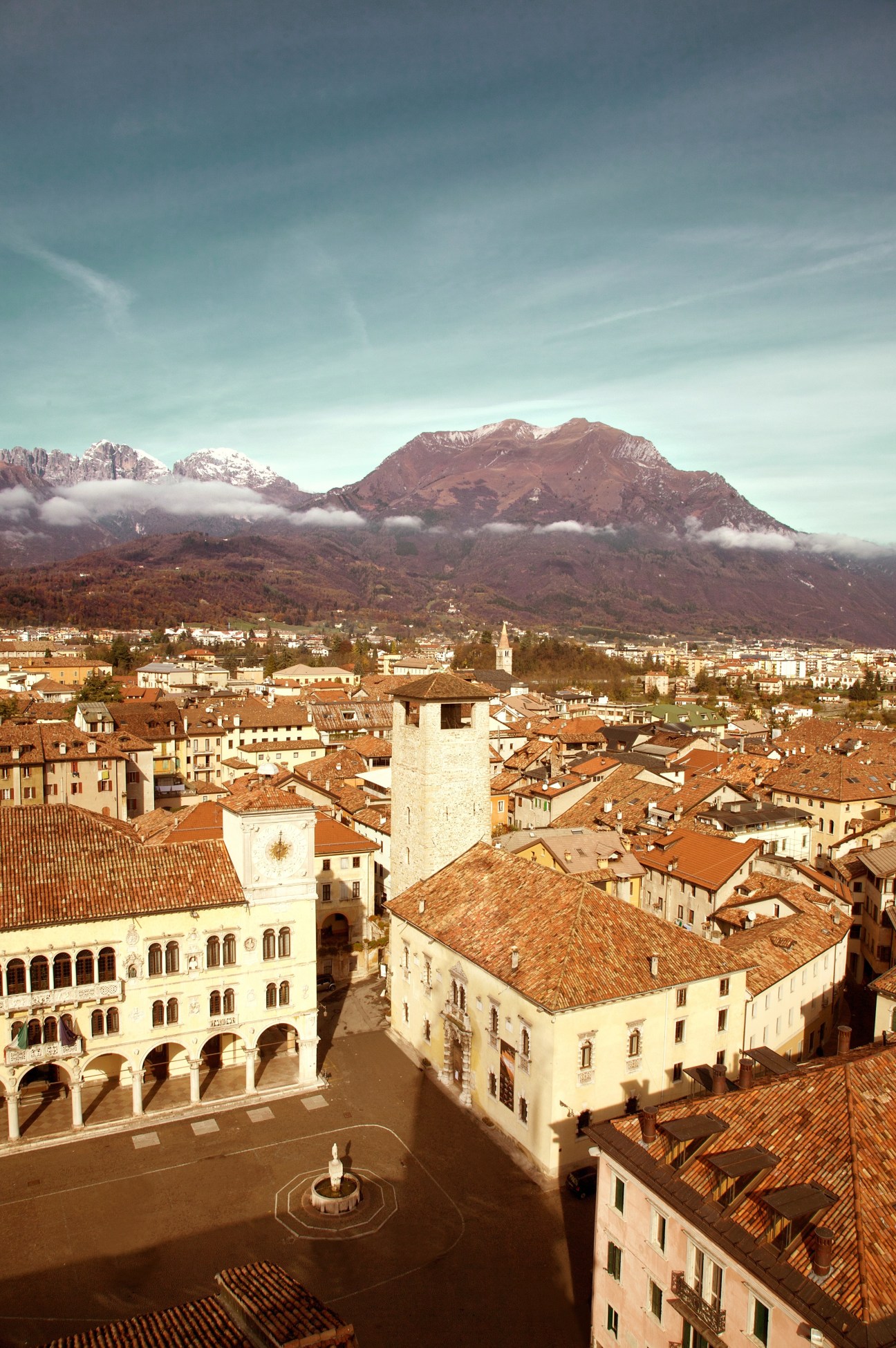 Aerial view of Belluno town with Dolomite mountains snow-capped in the background under blue sky.