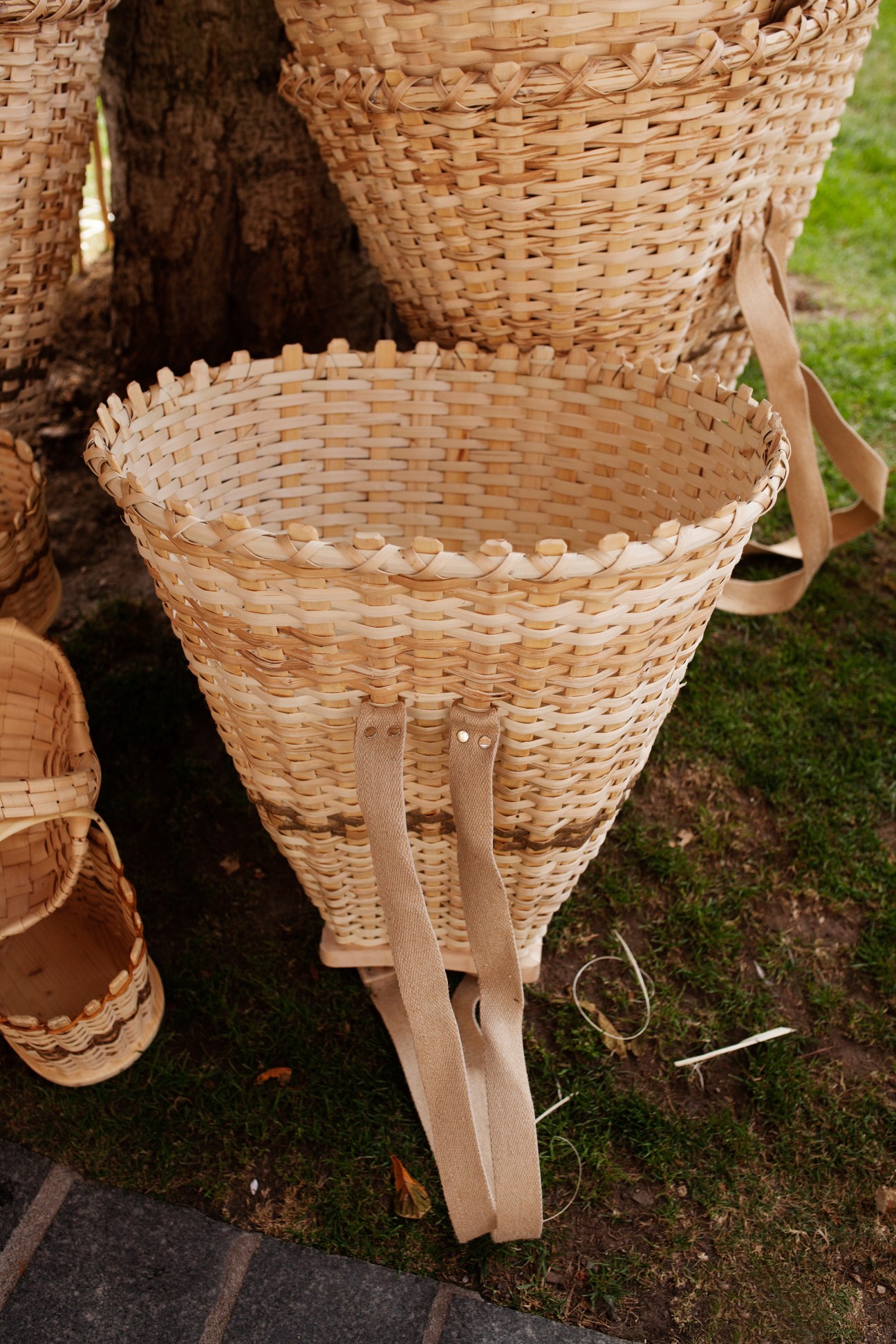 Traditional woven baskets with shoulder straps displayed on grass at outdoor craft festival