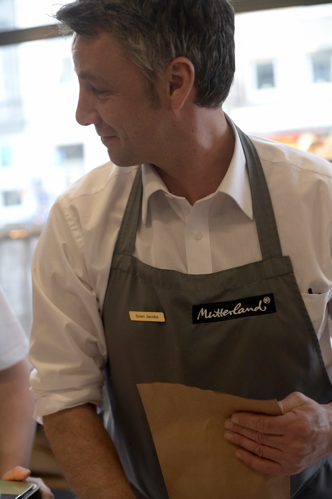 Mutterland staff member wearing an olive apron with the Mutterland logo, holding a brown paper package.